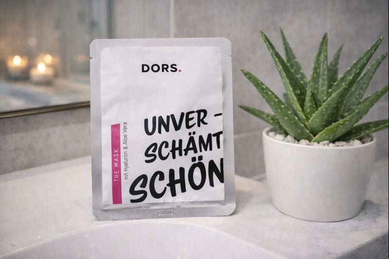 DORS „The Mask“ Gesichtsmaske steht im modernen Badezimmer neben einer Aloe-Vera-Pflanze – feuchtigkeitsspendende Tuchmaske mit Hyaluron und Aloe Vera für intensive Pflege und Glow.