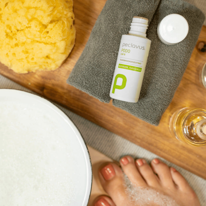 PECLAVUS Fußbadekonzentrat – 50ml, Flasche auf Handtuch liegend mit Naturschwamm und Wasserschale