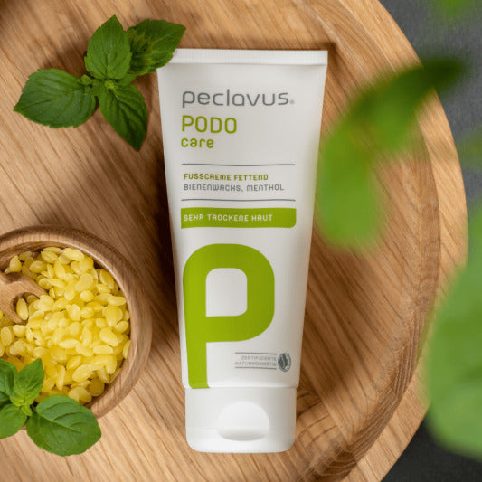 peclavus Fußcreme fettend – 100ml, Tiegel auf Holzteller liegend mit Bienenwachskugeln