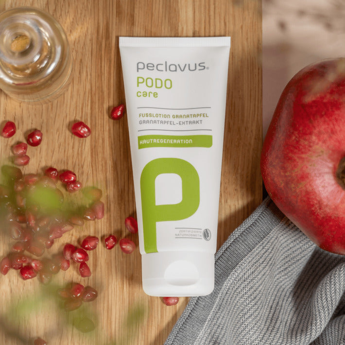 PECLAVUS Fußlotion Granatapfel – 100ml, Tube auf Holz liegend mit Granatapfelkernen