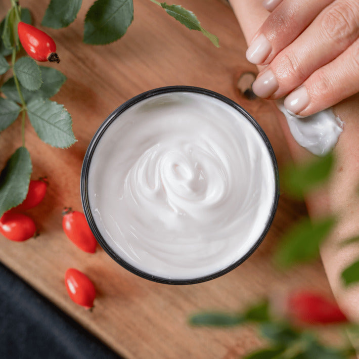 peclavus Körperbutter Wildrose – 250ml, Tiegel offen auf Holz stehend mit Hagebutten