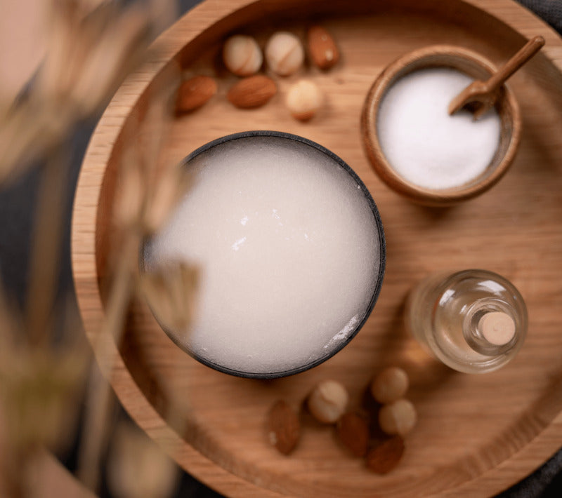 PECLAVUS Körperpeeling neutral – 500ml, Dose offen auf Holztablett mit Macadamianüssen