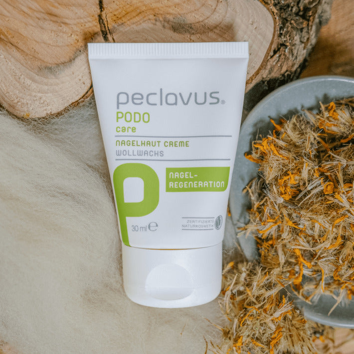 PECLAVUS Nagelhaut Creme – 30ml, Tube liegend auf Holz mit getrockneten Ringelblumen