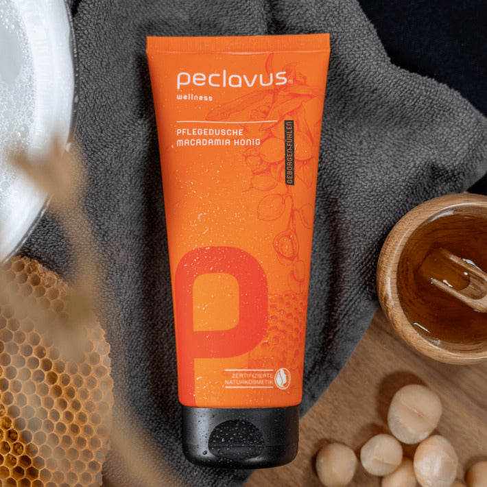 PECLAVUS Pflegedusche Macadamia Honig – 200ml, Tube auf Handtuch liegend mit Macadamianüssen