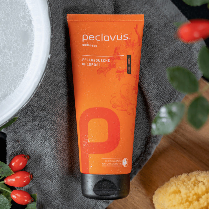 PECLAVUS Pflegedusche Wildrose – 200ml, Tube auf Handtuch liegend mit Hagebutten