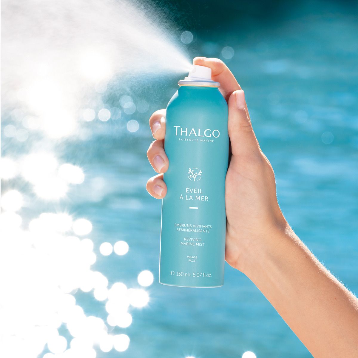 THALGO Éveil à la Mer - Remineralisierendes Meerwasser-Spray – 150ml, Hand betätigt Sprühkopf vor Meereshintergrund