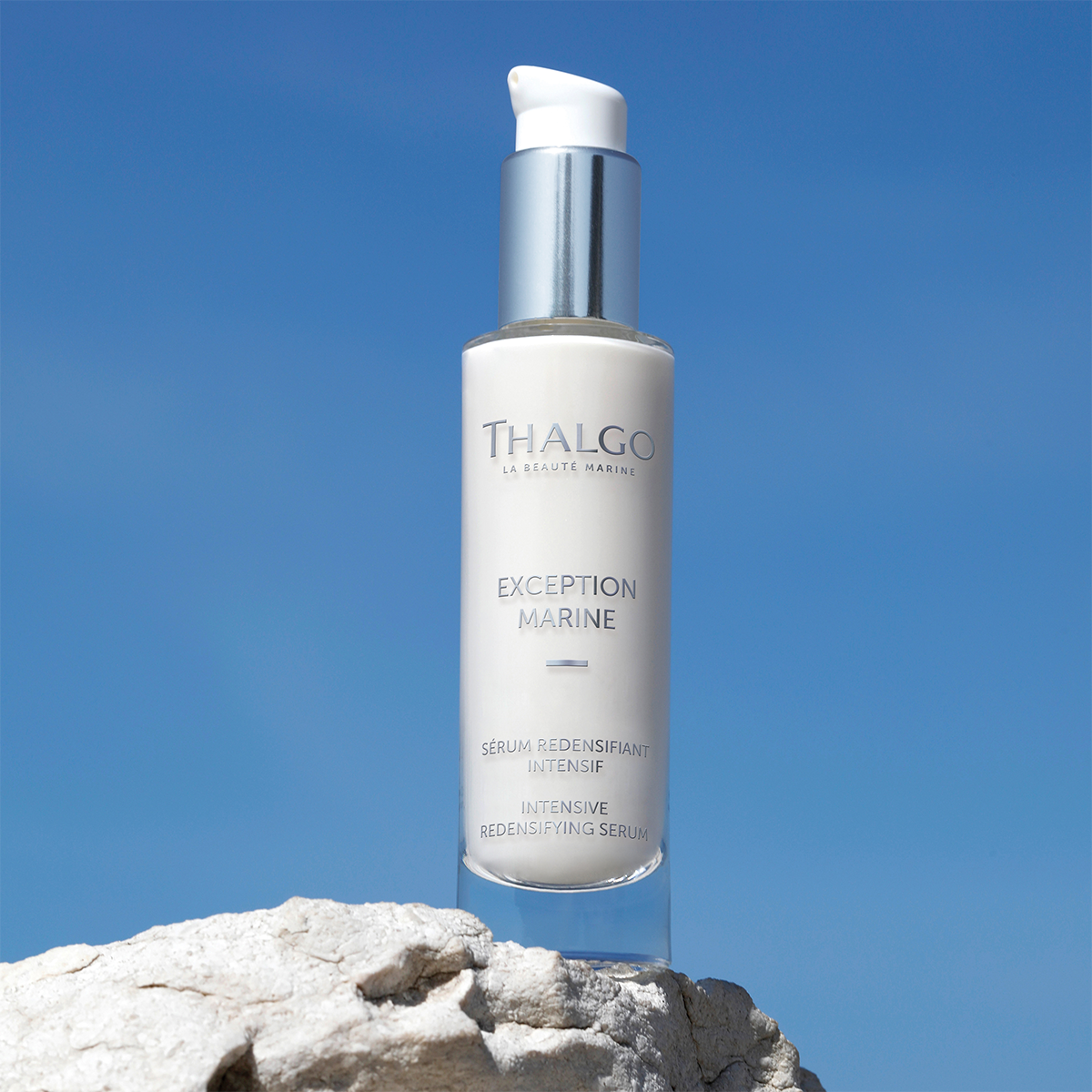 THALGO Exception Marine - Serum zur intensiven Festigung – 30ml, Flacon auf Stein stehend vor blauen Hintergrund