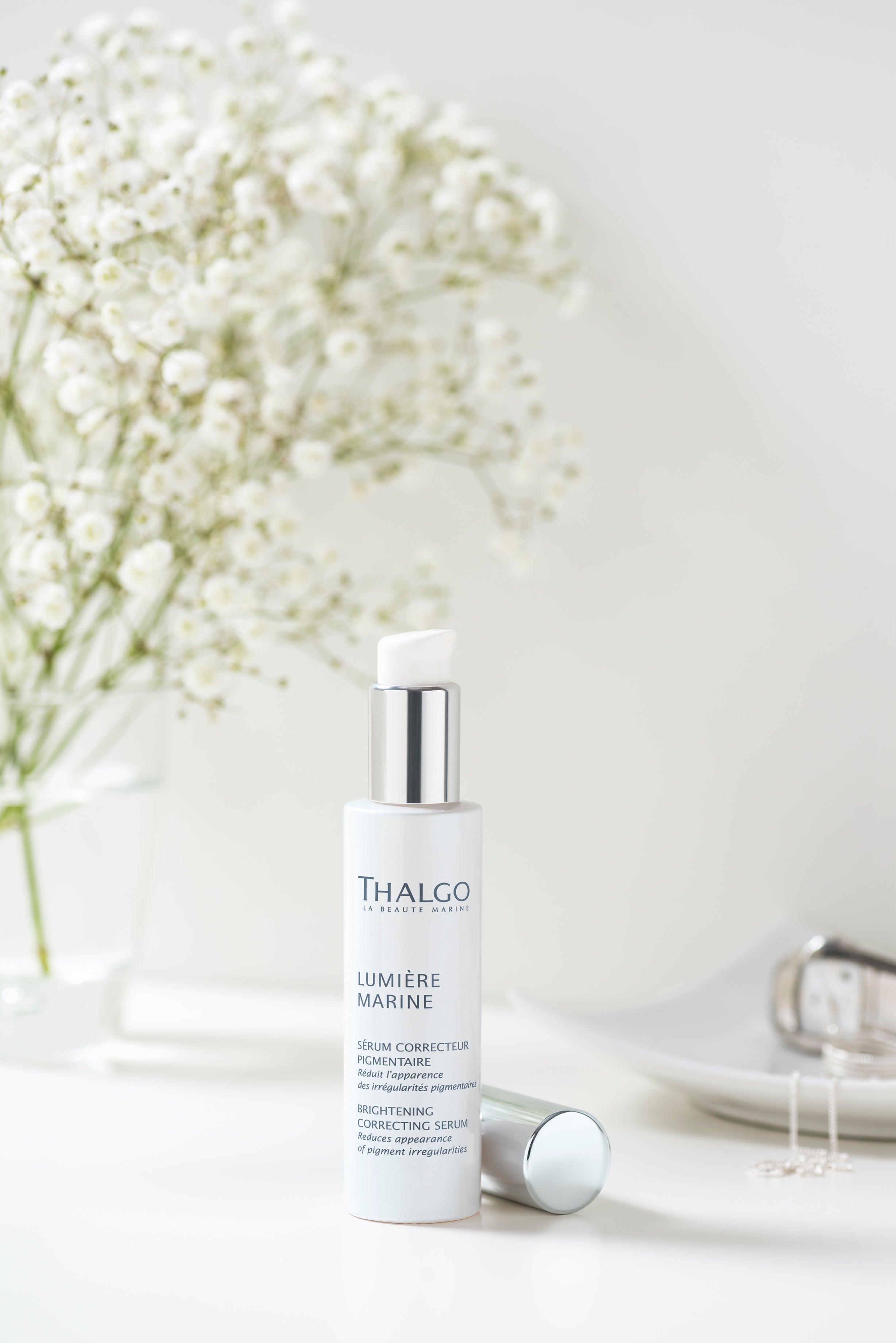 THALGO Lumière Marine - Brightening-Serum – 30ml, Spender auf weißem Tisch mit Schmuck und Blumenstrauß