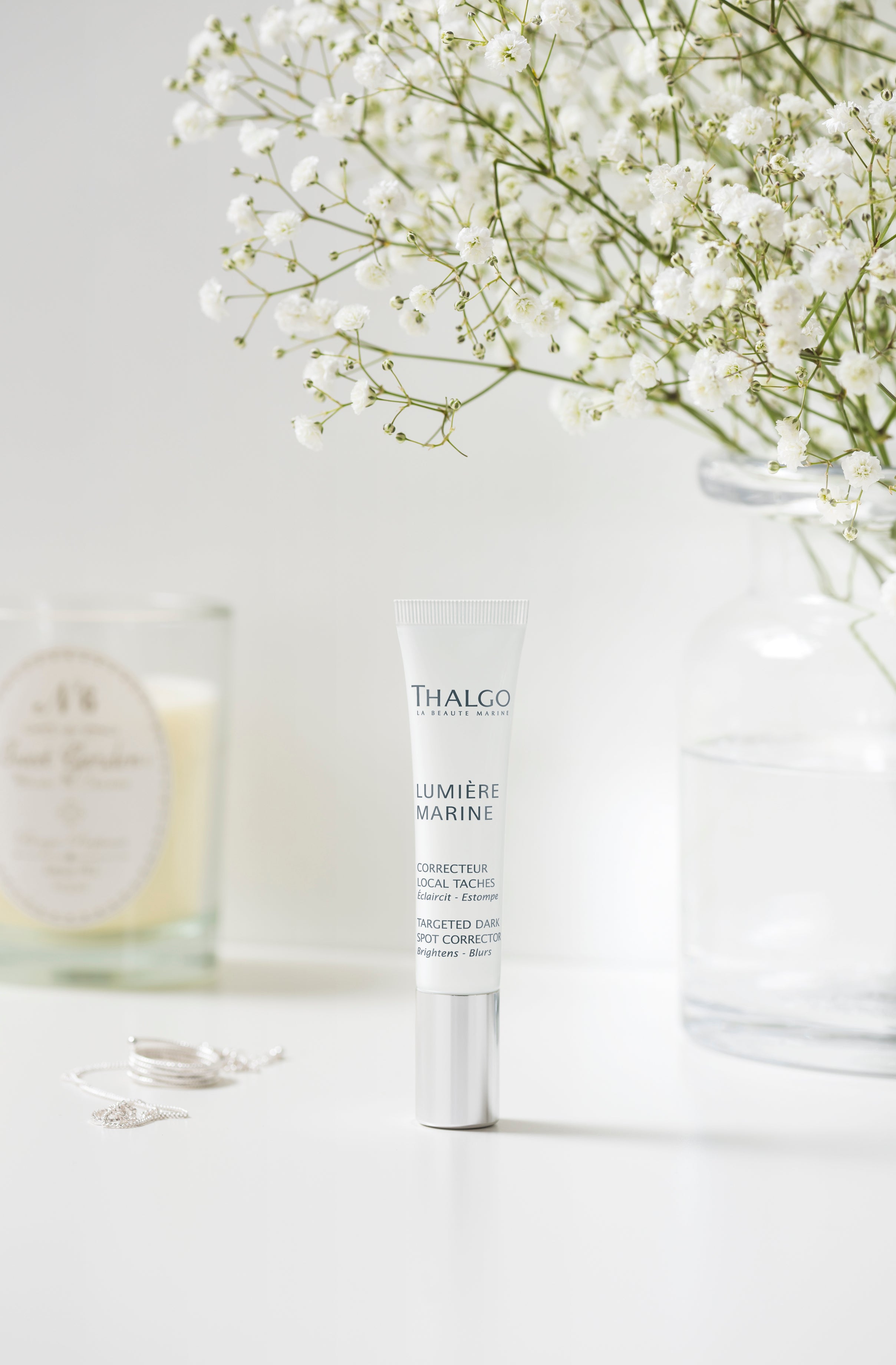 THALGO Lumière Marine - Korrekturstift gegen Pigmentflecken – 15ml, Tube auf weißem Tisch mit Schmuck und Blumenstrauß