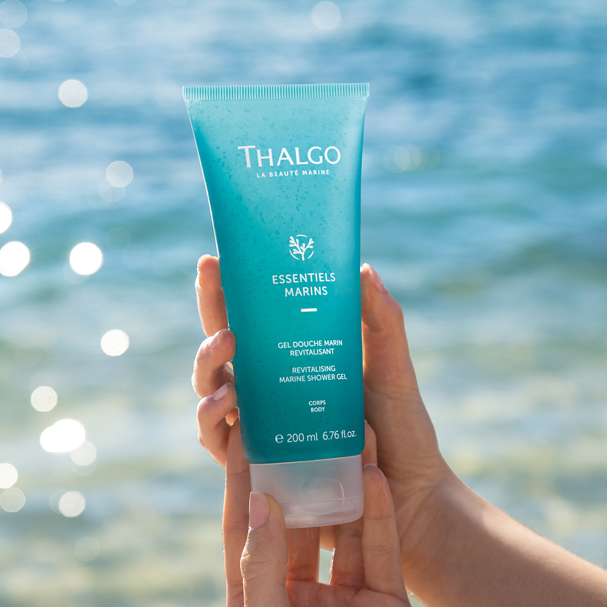 THALGO Marine Essentials - Revitalisierendes Duschgel  – 200ml, Hände halten Tube am Meeresstrand