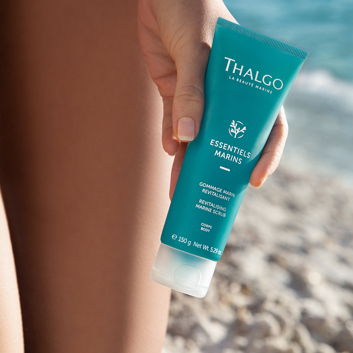 THALGO Marine Essentials - Revitalisierendes Körperpeeling – 150ml, Frau hält Tube am Strand