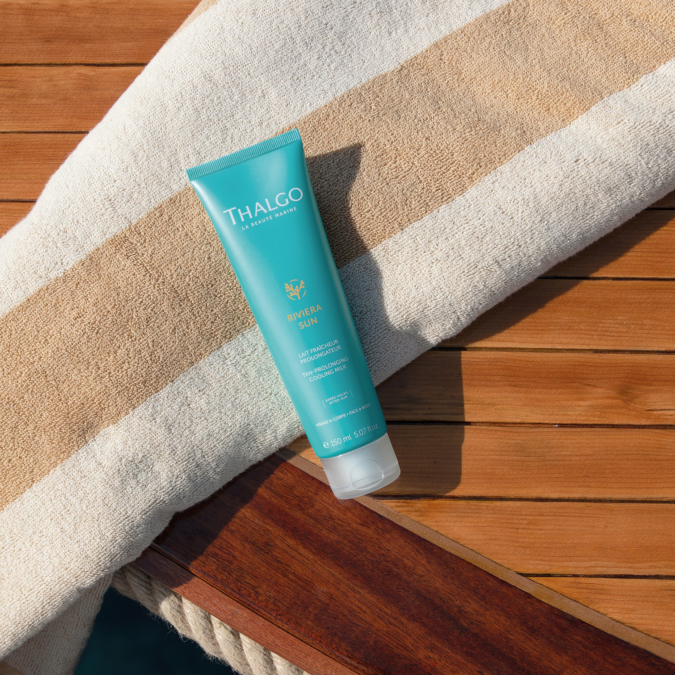 THALGO Riviera Sun Kühlende Aftersun-Lotion – 150ml, Tube liegend mit Handtuch auf Holzsteg