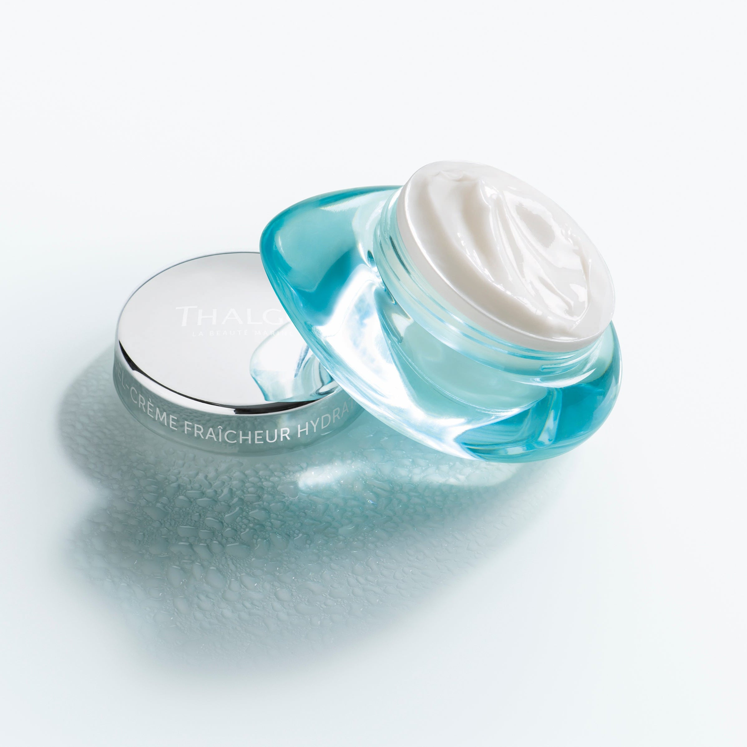 THALGO Source Marine - Kühlendes Feuchtigkeitsfluid – 50ml, Tiegel offen gegen Deckel gekippt auf Tisch mit Wassertropfen