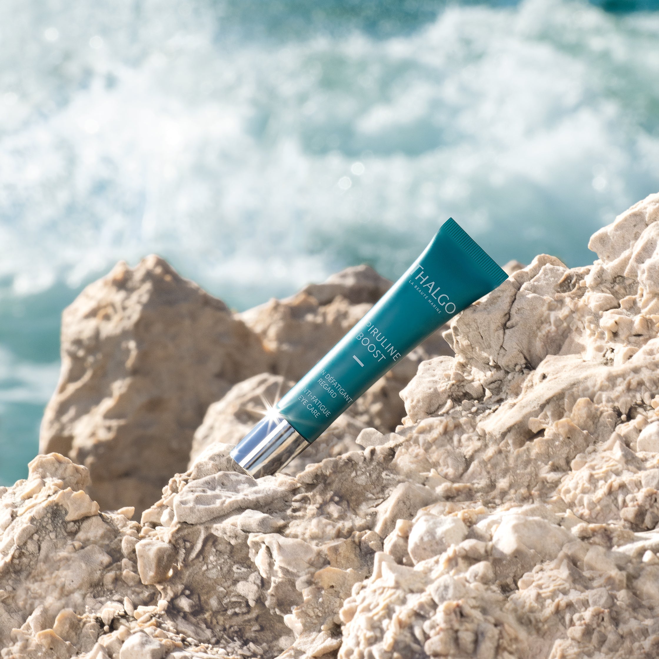 THALGO Spirulina Boost - Vitalisierende Augen-Pflege – 15ml, Tube auf Steinen liegend vor Meeresbrandung