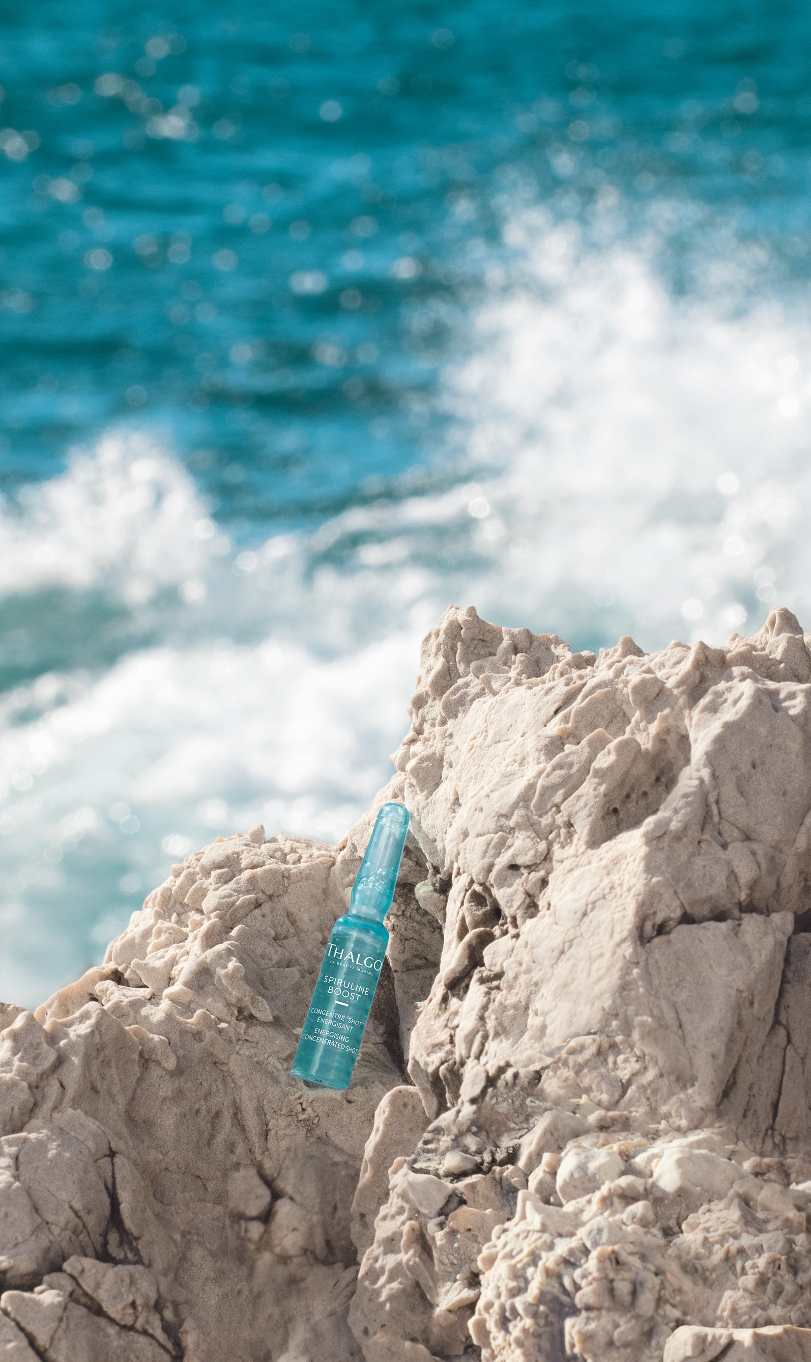 THALGO Spirulina Boost - Vitalisierendes Shot-Konzentrat – 1,2ml, Einzelampulle auf Steinufer am Meer