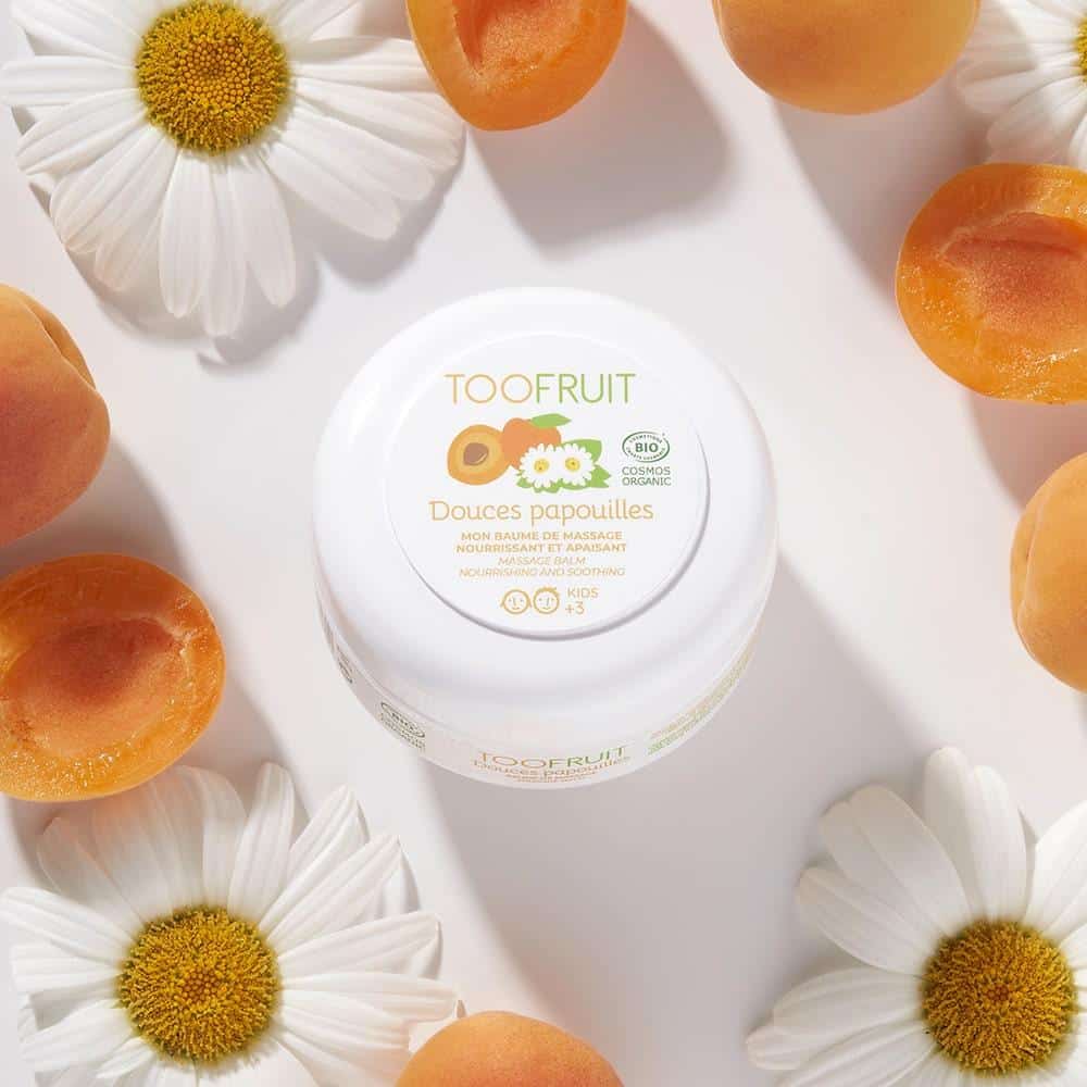 TOOFRUIT Douces Papouilles Massagebalsam – Aprikose-Kamille, 75ml, Tiegel umringt von Kamillenblüten und Aprikosen