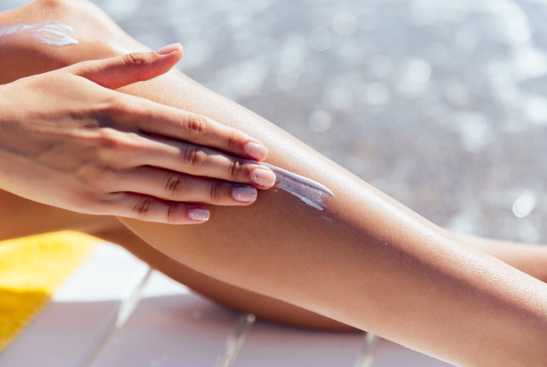 Hand trägt eine weiße Creme auf die Haut am Unterschenkel zwischen Knie und Knöchel auf.
