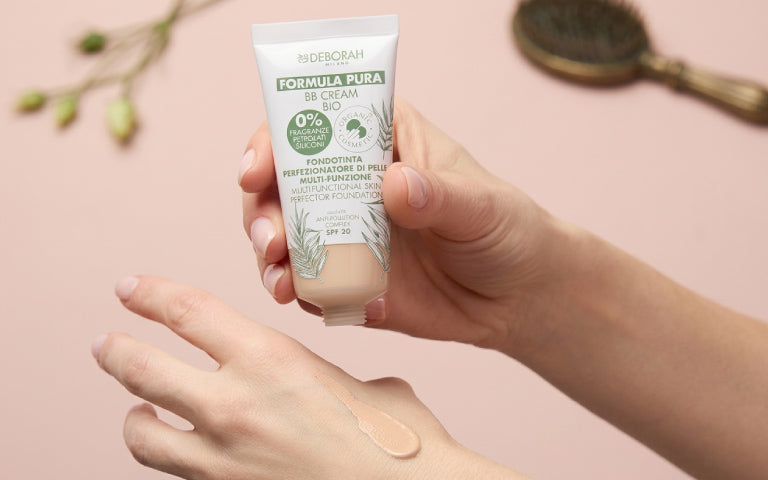 Weibliche Hände halten die geöffnete Tube des BB Cream Formula Pura von Deborah. Auf dem Handrücken der anderen Hand ist eine kleine Menge der BB Cream aufgetragen.