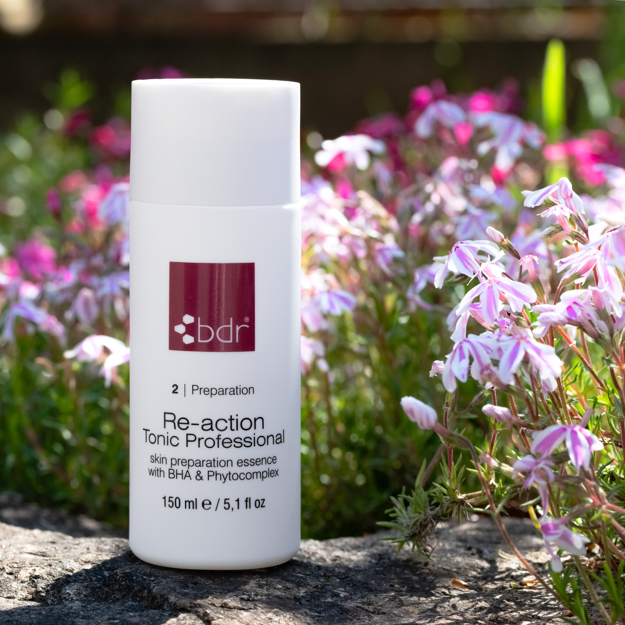 beautymanufactur-bdr-medical-beauty-re-action-tonic-professional-150ml-bdr-11419229-3-flasche-steht-auf-einem-stein-vor-blumenhintergrund
