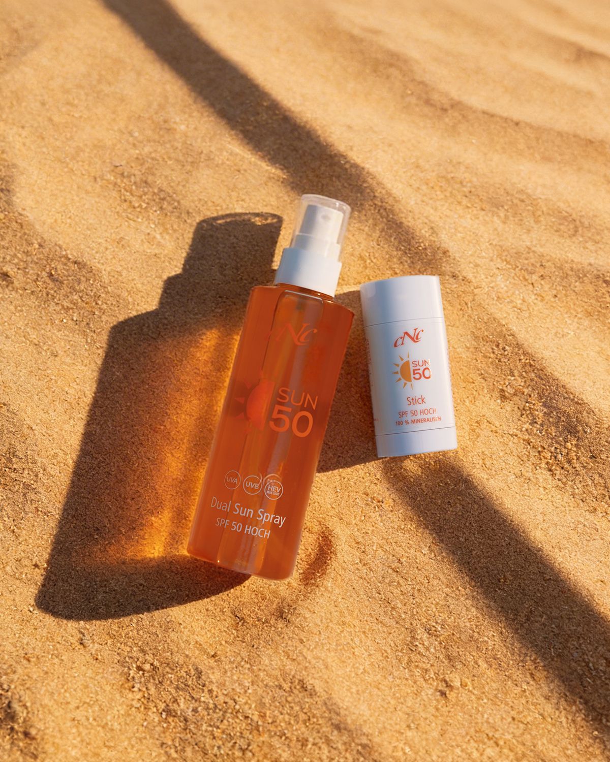 CNC SUN Stick SPF 50  – mineralischer Sonnenschutz für unterwegs, 35g, Stick und Sonnenspray auf Sand liegend