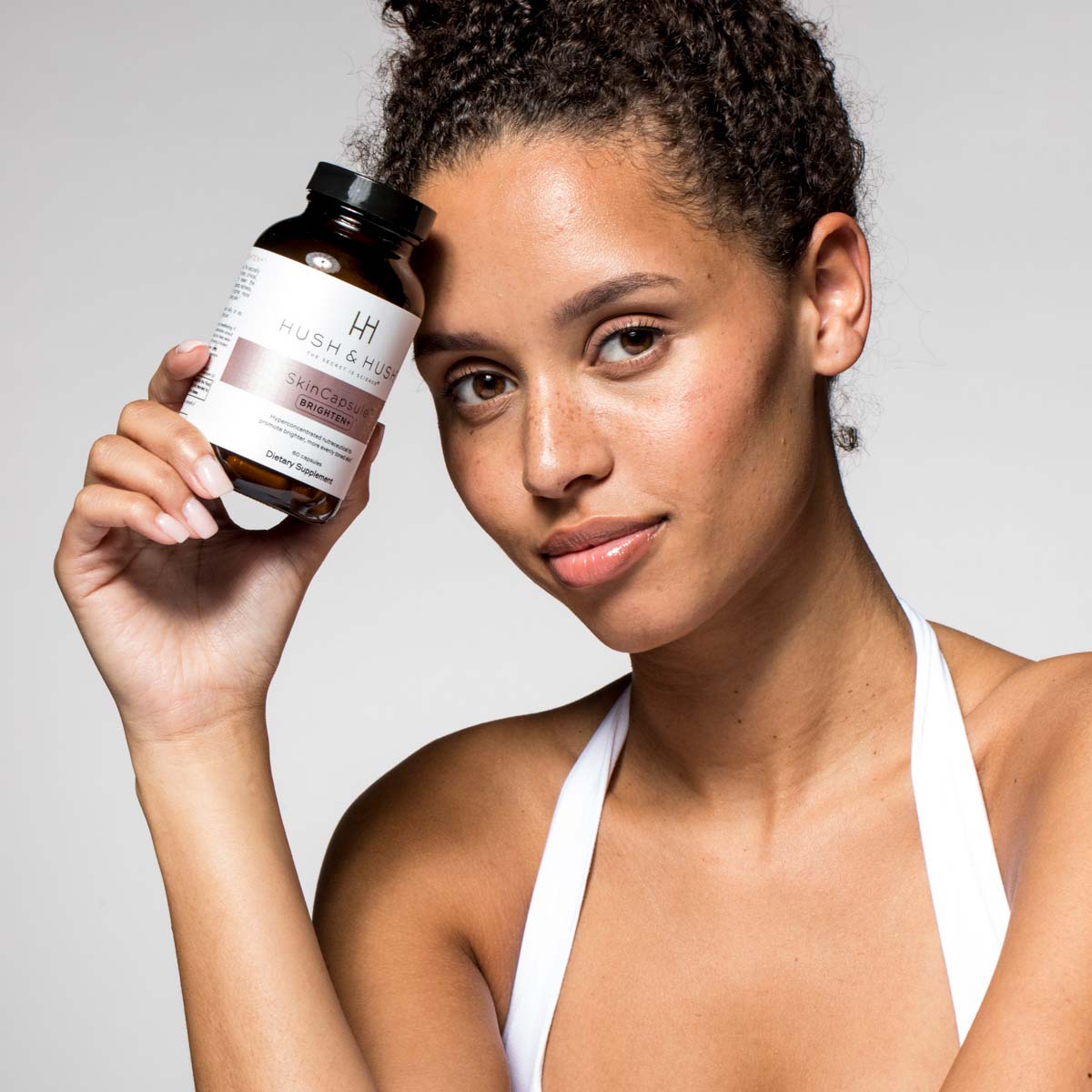 HUSH & HUSH Skincapsule™ Brighten+ – Nahrungsergänzungsmittel, 50g, Frau hält Dose