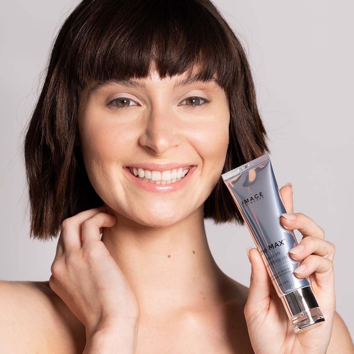 IMAGE SKINCARE the MAX Neck Lift  – Pflege für Hals und Dekolleté, 59ml, Frau hält Tube neben Gesicht