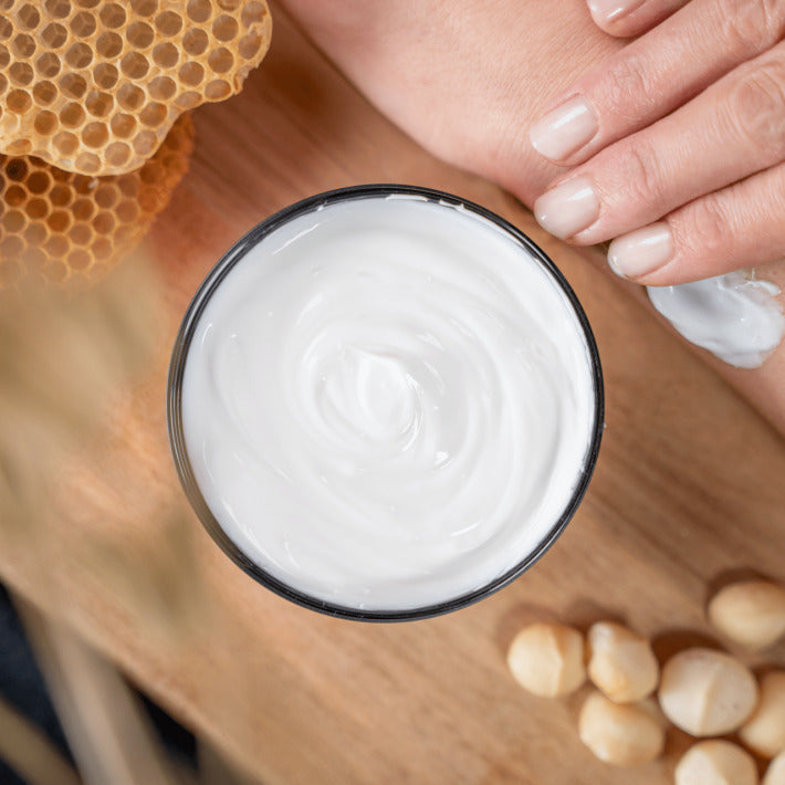 PECLAVUS Körperbutter Macadamia Honig  – 250ml, Tiegel offen auf Holz stehend mit Nüssen und Honigwabe