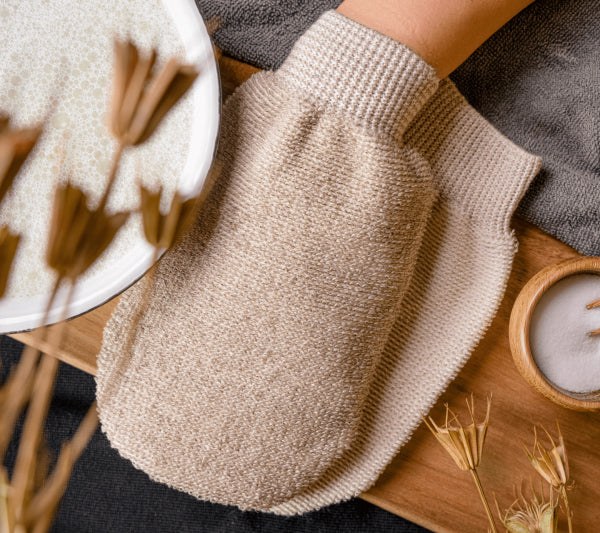 PECLAVUS Peeling- und Massagehandschuh – ., liegend auf Holz neben Wasserschale