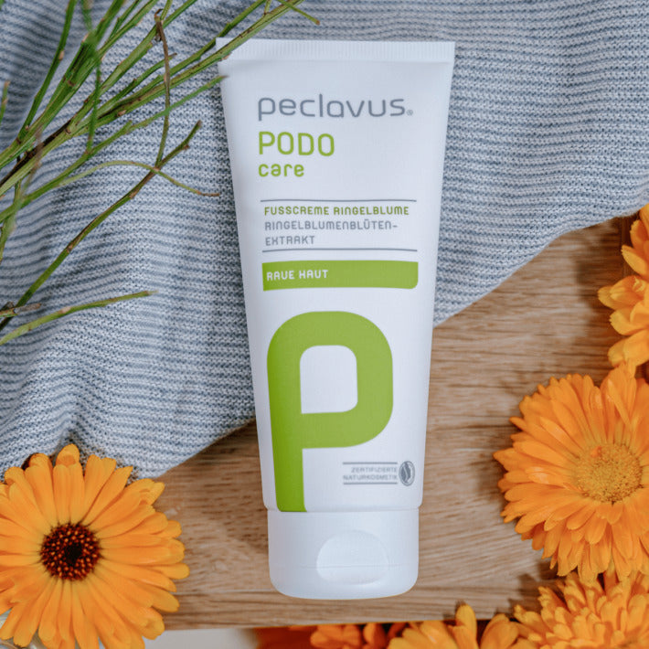 PECLAVUS ußcreme Ringelblume  – 100ml, Tube auf Holz und Stoff liegend mit Ringelblumenblüten