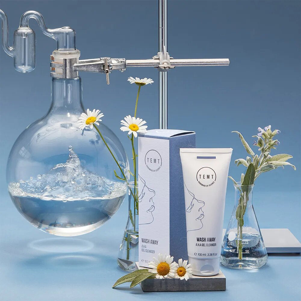 TEMT Wash away A.H.A Gel Cleanser  – 100ml, Tube und Umkarton mit Kamillenblüten und Laborutensilien
