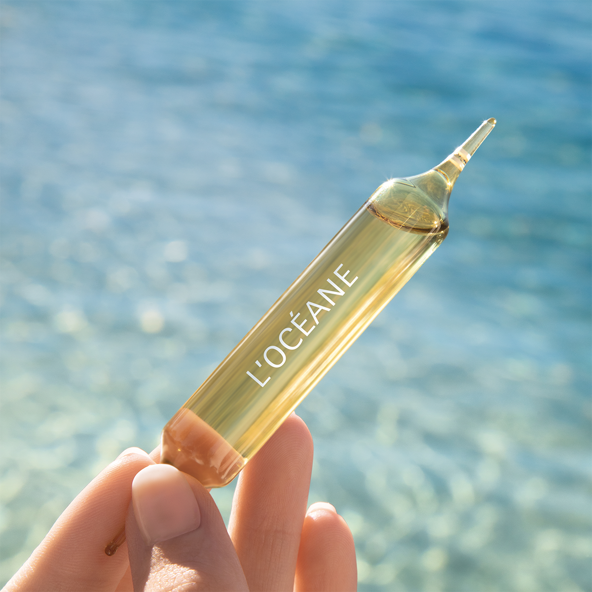THALGO L'Océane Trink-Ampullen  – Nahrungsergänzung, 10ml, Hand hält Einzelampulle mit Meereshintergrund