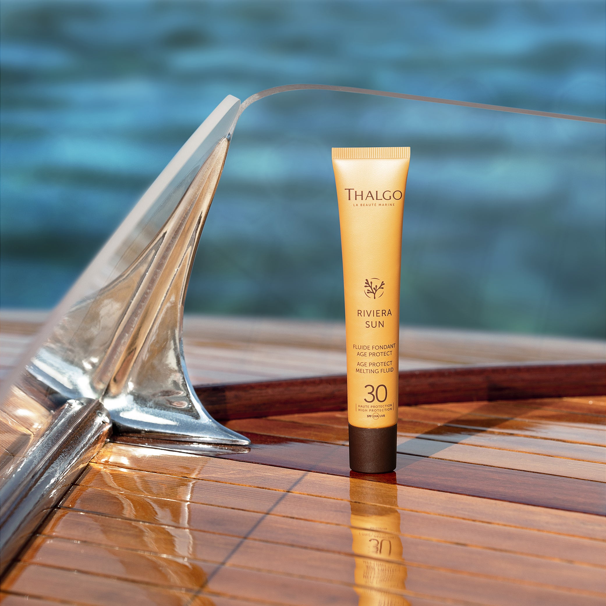 THALGO Riviera Sun Age-Protect Sonnenschutz-Fluid  – LSF 30, 50ml, Tube stehend auf Holzboot im Wasser